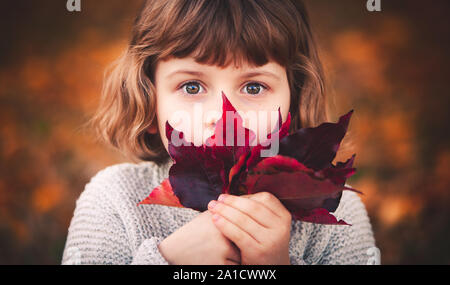 Wenig kaukasische Mädchen ist, die Ihr Gesicht mit einem Blatt und gerade mit Blick auf die Kamera Stockfoto