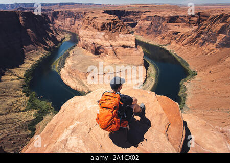 Mann mit einem Rucksack sitzt auf dem Rock und entfernt mit Blick auf die Horseshoe Bend, AZ Stockfoto