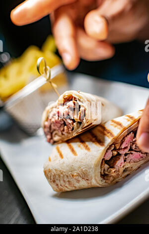 Ein gegrilltes Steak Tortilla Wrap Neben einer Portion Pommes Frites angesichts der letzten Schliff von einem Koch, Stockfoto