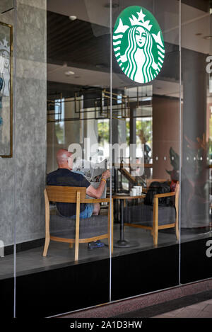 Starbucks Restaurant durch die Fenster mit einem Mann die Zeitung liest und einen Kaffee. Stockfoto