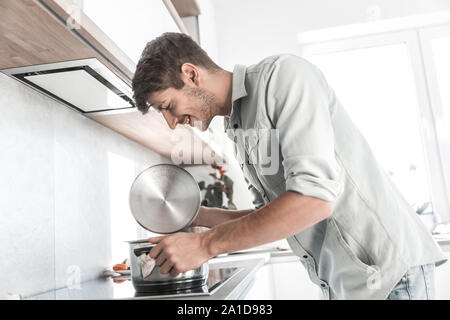 Aus der Nähe. Ein lächelnder Mann sieht in einen Topf von Lebensmitteln Stockfoto