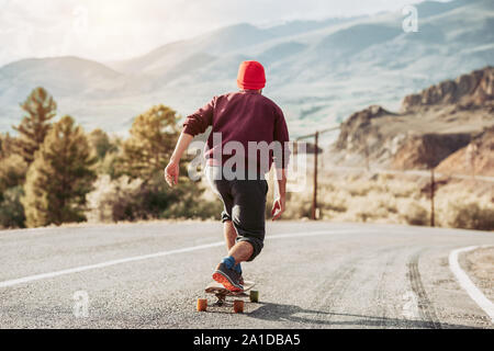 Mann Hipster ist Skateboarding bei Mountain Road im Abendlicht Stockfoto