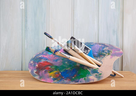 Holz Palette mit Farben und Pinsel auf farbigen Holz- Hintergrund Stockfoto