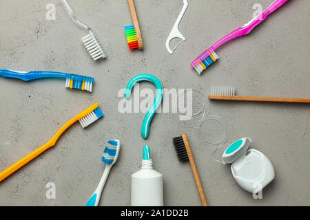 Zahnpasta in Form eines Fragezeichens und viele verschiedene und farbigen Zahnbürsten und Zahnseide. Konzept der, wie man die richtige Zahnbürste oder wie Sie Ihre Zähne zu putzen. Stockfoto