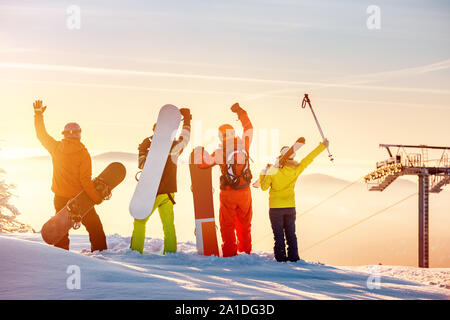 Gruppe der glücklichen Freunde Skifahrer und Snowboarder steht bei Sonnenuntergang Mountain Top und Spaß Stockfoto