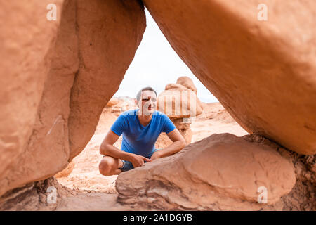 Mann Wanderer hinter dem Rahmen des hoodoo Sandstein Felsformationen glücklich lächelnde Wüstenlandschaft im Goblin Valley State Park in Utah sitzen auf der Spur Stockfoto