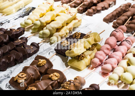 Früchte, Bananen, Erdbeeren, Nüsse, Äpfel, Pfirsiche in weißer und dunkler Schokolade getaucht. Stockfoto