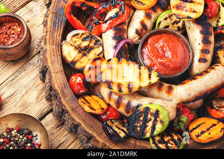 Gegrillte Würstchen und Gemüse mit Sauce Ketchup auf einem Holztisch. Herbst essen Stockfoto