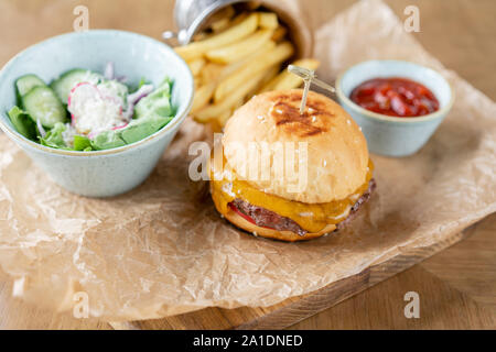 Cheeseburger mit Salat, Tomaten, Pommes frites und geschmolzenem Käse. Der Tisch im Restaurant. Ungesunde Lebensmittel. Stockfoto