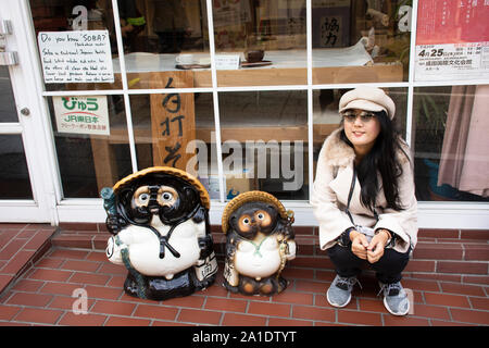 Reisende Thai Frauen portrait posiert für ein Foto mit japanischen Marderhund oder Tanuki in Naritasan Omote Sando oder Narita Altstadt in Chiba auf März Stockfoto