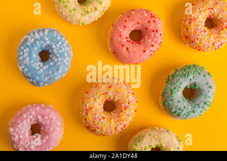 Farbige Donuts, Gebäck auf gelbem Hintergrund, Ansicht von oben. Stockfoto