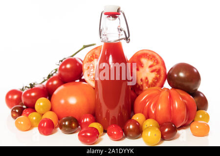 Eine Menge von verschiedenen Tomaten und eine volle Flasche mit Saft oder Tomatensoße, vor weißen Stockfoto