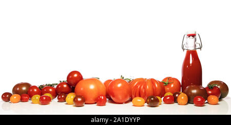 Eine Menge von verschiedenen Tomaten und eine volle Flasche mit Saft oder Tomatensoße, vor weißen Stockfoto