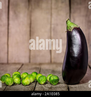 Frische Auberginen und Rosenkohl vor einem rustikalen Holzmöbeln Hintergrund Stockfoto