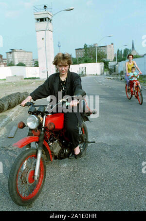 04 April 1990, Berlin, Mitte: Eine junge Frau Antriebe am 4.4.1990 mit ihrem Moped Simson S50 im ehemaligen Mauerstreifen an der North Station und Praktiken für das Moped testen. Im Hintergrund ein ehemaliger Wachturm der DDR-Grenztruppen. Bestmögliche Bildqualität. Foto: Thomas Uhlemann/zentralbild - dpa/ZB Stockfoto