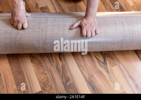 Des Menschen Hand mit einem neuen Teppich auf dem Boden gerollt, Verpackungen aus Kunststoff Stockfoto