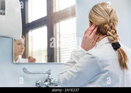 Ärztin schaut in den Spiegel im Badezimmer müde Stockfoto