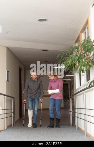 Zwei Personen mit Gips am Bein und Arm, männlich ist Laufen mit Krücken Stockfoto