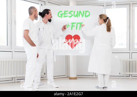 Medizin Personal steht vor einer Tafel, auf der die deutschen Wörter gesund und fit Das bedeutet gesund. Ein rotes heartsymbol unter ihnen. c Stockfoto