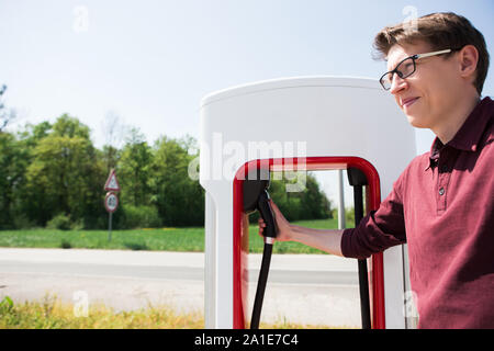 Ein Mann steht hält einen Stecker der Kompressormotoren für ein Elektrofahrzeug Stockfoto