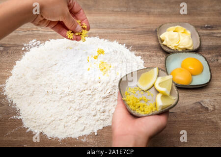 Frau, die zitronenschale auf Mehl, Butter und Eier auf der Seite, Cookie und Keks Bäckerei Stockfoto