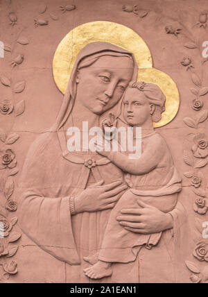 Skulptur in Flachrelief in roten Stein von Maria und Jesuskind, mit goldenen Kronen. Ideal für Konzepte, Ereignisse und Hintergründe. Stockfoto