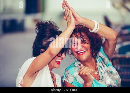 Gerne ältere weibliche Freunde geben High Five, Erfolg feiern, während Sie einander sitzen, die in der Tabelle in einem Café im Freien. Stockfoto