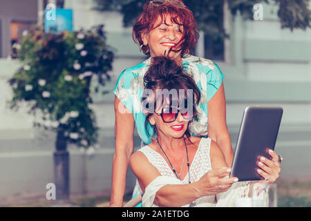 Zwei glückliche älterer Frauen mit Tablet und beobachten Media Content online, während in einem Café im Freien sitzen. Stockfoto