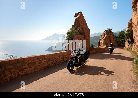 Motorradfahren die schmale kurvenreiche Küstenstraße durch die rosig-rot verwitterte Granitfelsküste des Golfs von Porto in Korsika Frankreich. Stockfoto