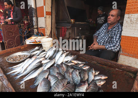 Alexandria, Ägypten - Dezember 18, 2018: Fisch Verkäufer sitzt in der Nähe der Zähler mit einem Fisch auf einem im Markt Stockfoto