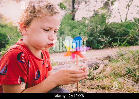 Wenig schöner Junge bläst ein Windrad in einem Wald, sorglos, mit verblassten Farben und Retro Style. Stockfoto