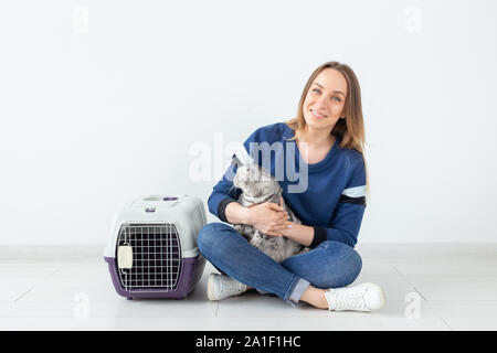 Charmante positive junge Frau hält in ihrer Hände ihre schönen grauen schottischen Katze sitzt auf dem Boden in eine neue Wohnung. Pet-Konzept. Stockfoto