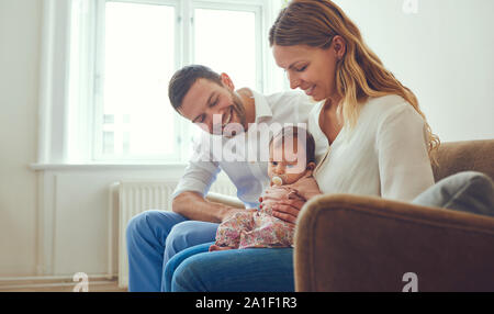 Lächelnde junge Mutter und Vater auf dem Sofa im Wohnzimmer zusammen zu Hause sitzen mit ihrer süßen kleinen Tochter Stockfoto