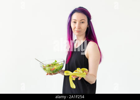 Junge Asiatin hipster coloriertes Haar in den Händen halten, ein Maßband mit Salat posiert auf weißem Hintergrund mit Copyspace. Gesund Stockfoto