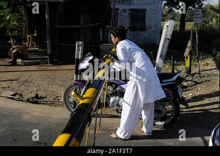 Indien, Madhya Pradesh, Nimad region, Khargone, Motorrad fahrer verletzen Verkehrsregeln während ein Bahnübergang Kreuzung mit geschlossenen Schranken Stockfoto