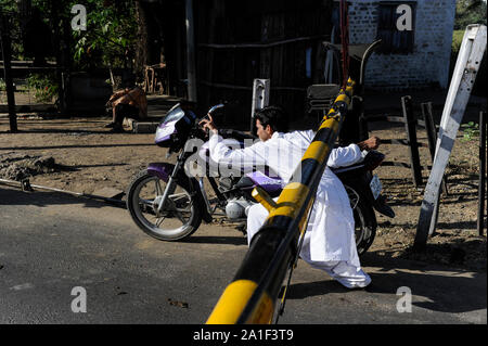 Indien, Madhya Pradesh, Nimad region, Khargone, Motorrad fahrer verletzen Verkehrsregeln während ein Bahnübergang Kreuzung mit geschlossenen Schranken Stockfoto