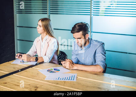Langweilige Präsentation. Gruppe junger Geschäftsleute in Smart Casual Wear gelangweilt beim zusammen am Tisch sitzen und Wegsehen. Stockfoto