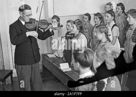 Der Lehrer begleitet seine Schulkasse in der Schule von Horka beim Singen mit seiner Geige im Musikunterricht, Deutschland 1949. Lehrer begleiten seine Klasse mit seiner Geige, während an der Schule von Dortmund, Deutschland 1949 singen. Stockfoto