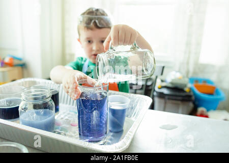 Elementare alter Junge gießt Wasser in ein Glas während Du einen Stamm Projekt Stockfoto