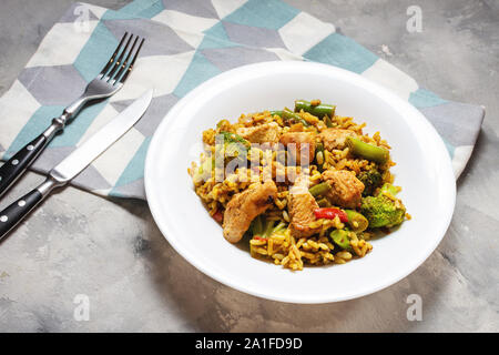 Reis mit Hühnerfleisch und Gemüse in eine Platte auf konkrete Tabelle Stockfoto