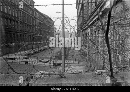 Blick durch Stacheldraht auf der Mauer in eine Straße im Ostteil der Stadt, Deutschland 1962. Blick durch Stacheldraht auf der Berliner Mauer zu einer Straße im Ostteil der Stadt, Deutschland 1962. Stockfoto