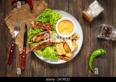 Gegrillte Shish Kebab mit Bratkartoffeln und Sauce auf hölzernen Hintergrund serviert. Ansicht von oben Stockfoto