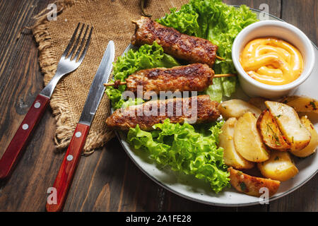 Gegrillte Shish Kebab mit Bratkartoffeln und Sauce auf hölzernen Hintergrund serviert. Stockfoto