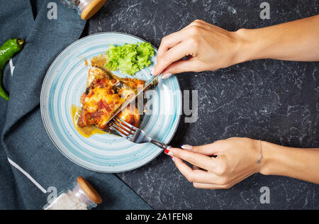 Weibliche Hände halten Sie Messer und Gabel. Gebackene Auberginen mit Käse auf einem Tisch aus Stein. Parmigiana melanzane. Ansicht von oben. Stockfoto