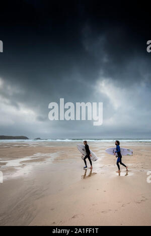 Surfer gehen auf den Fistral Beach als dunkle, düstere Gewitterwolken in Newquay in Cornwall. Stockfoto