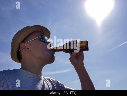 Attraktiver Mann in einen Hut erhalten Sie erfrischende Getränke und kühles Bier aus der Flasche draußen vor blauem Himmel Stockfoto