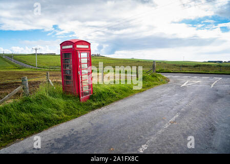 Lonely traditionelle britische Telefonzelle in der Nähe einer Kreuzung in der Landschaft auf einem leicht bewölkt Frühling Stockfoto