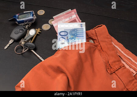 Euro Papiergeld und Münzen fielen aus der Tasche auf einem Schwarzen Tisch, auf dem eine Reihe von Haus und Auto Stockfoto