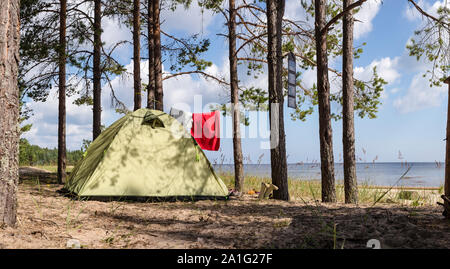 Panoramablick auf Zelt steht in einem Pinienwald am Meer in der Nähe der Sandstrand, beim Campen. Den Bäumen hängenden Kleidungsstücken und Solarkollektoren. Stockfoto