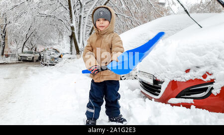 Bild von Boy clean up Schnee Auto nach Schnee fallen mit großen blauen Schaufel. Im kalten Winter morgen Stockfoto